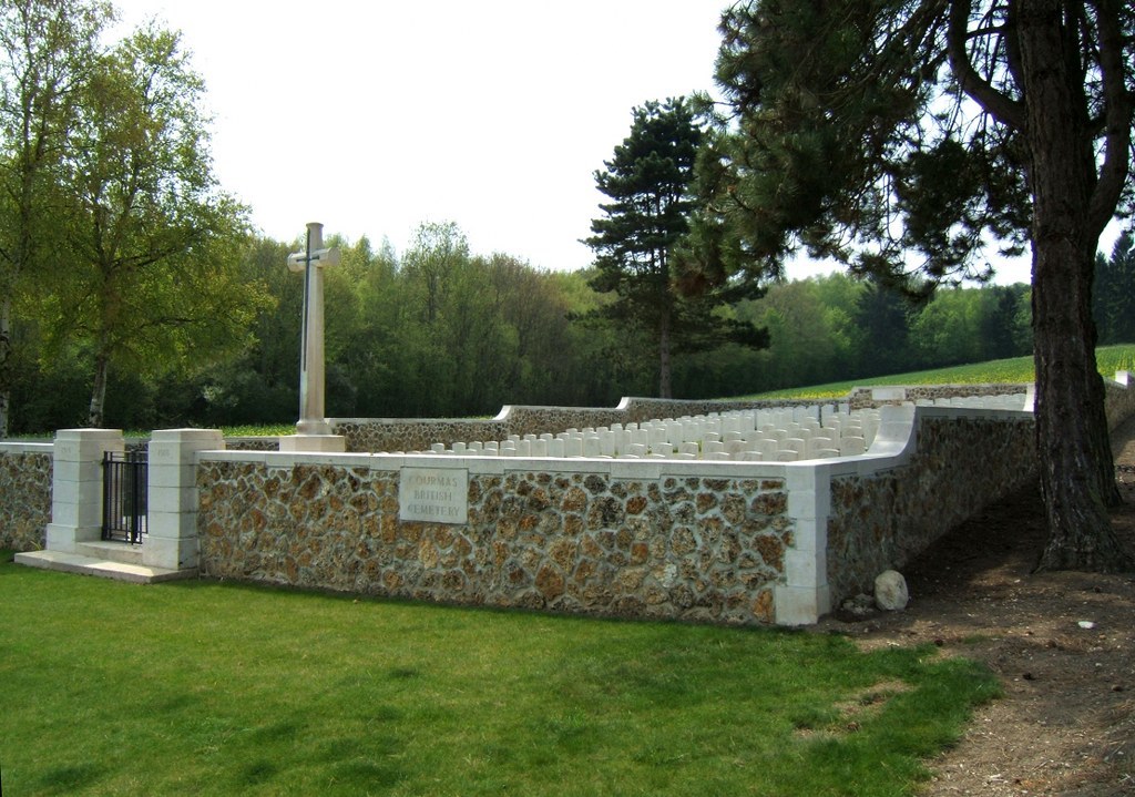 The graveyard of Courmas British Cemetery surrounded by a stone wall and trees