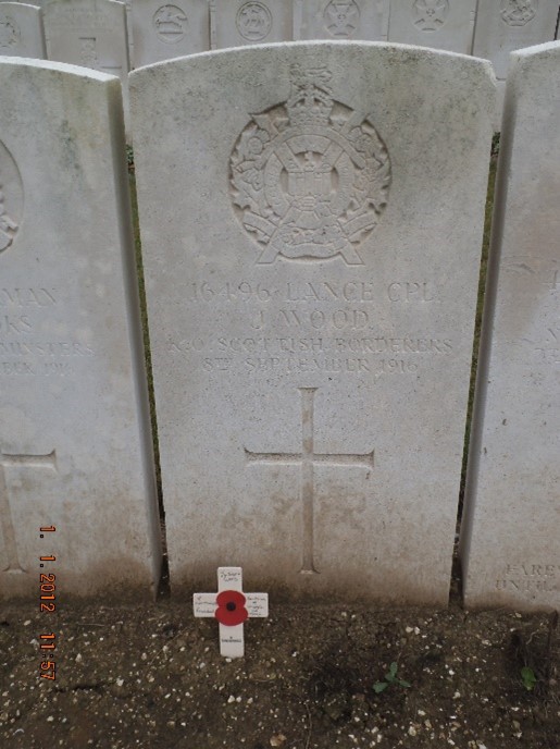 the white gravestone inscribed with his regiment's badge his details and a cross. a smaller wooden cross has been planted in front