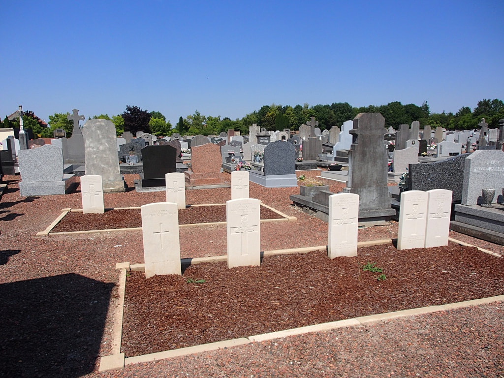 Eight white gravestones are separated form the greygravestones of the rest of the cemetery that surround them