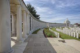 Photo of Tyne Cot Memorial. A row of columns that starts to the left and curves round the back of rows of white headstones.