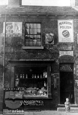 J.C.Lambert shop, Eastmoor A black and white photograph showing the premises of J.C.Lambert, confectioner and tobacconist, in Eastmoor. On the wall are old advertising posters. In the window, jars of sweets can be seen. The building later became part of the Fox and Grapes public house. Internal Reference: WR (LS) Frith Collection