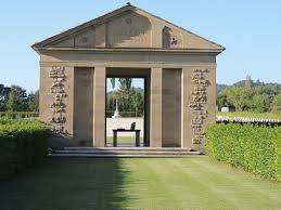 a large stone arch surrounded by low hedges leads to the cemetery where some gravestones can be seen