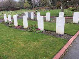 Photo of Leeds (Lawns Wood) Cemetery. Grassed area with rows of white headstones with plants in front.