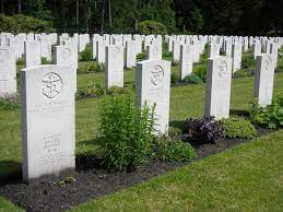 close up of rows of white gravestones with strips of grass between the rows and plants planted in front of the gravestones