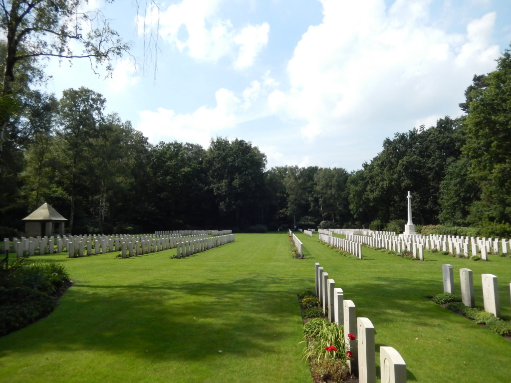 Rows of white gravestones within mown grass surrounded by trees