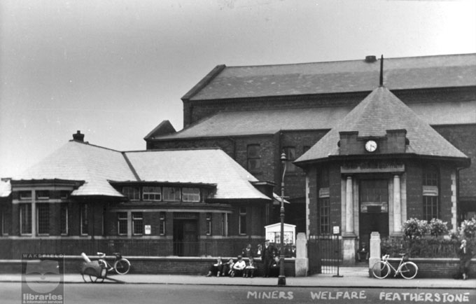 Old Featherstone Library and Miners' Welfare A black and white photograph showing Featherstone old library, Green Lane, Featherstone, prior to its closure in 1985. On the 4th September of the same year a new library and community centre was built on Station Lane. The image also shows the Miners' Welfare building which was used for social events such as dances. Internal Reference: Featherstone Green Spot No 46