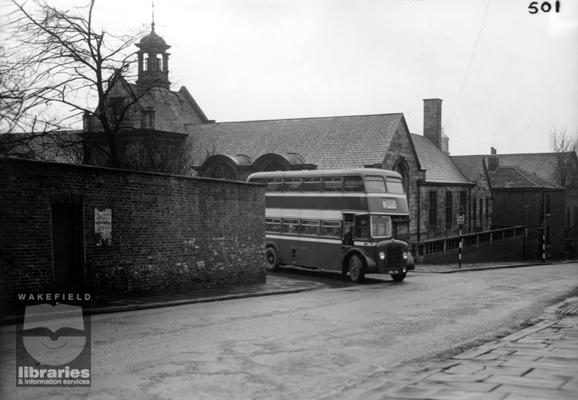 A view of Drury Lane and Back Lane, Wakefield, before improvements, 1956 A black and white photograph from the Wakefield City Engineers Collection showing Back Lane and Drury Lane, Wakefield, before the demolition of the wall on the right. The photograph was taken on Tuesday 1st May 1956 and shows a bus emerging from Drury Lane. Drury Lane Library is in the background, with Westgate Chapel on the far right. Internal Reference: WYAS WND (B208) 3/2