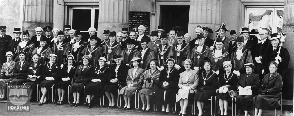 A black and white photograph taken outside the Borough of Beverley Guild Hall.  The Mayor Wakefield, Mr A.G.Webster is third from right in the middle row.  Other Mayors and Mayoresses, as well as mace bearers and several other local officials, possibly judges, are in the gathering.  The eighteenth century Guild Hall ceased to be a civic building in the late twentieth century, becoming the Beverley Guildhall Community Museum.  Internal Ref: WR