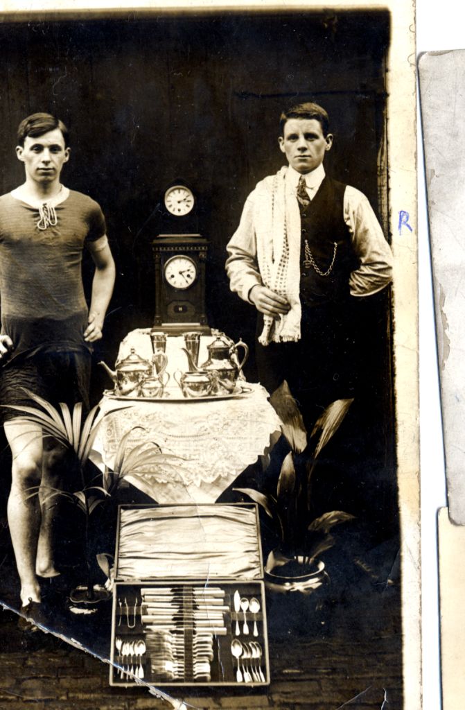 john and another man wearing his running clothes and posing beside his many prizes won for running