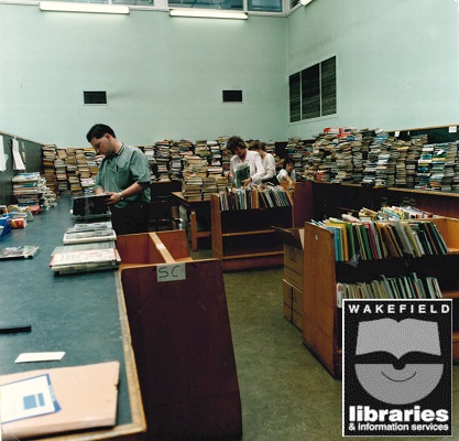 A colour photograph of staff working in the Circulation Department at Wakefield Library Headquarters, Balne Lane, Wakefield. The piles of books on the counter are known as "the hump" and are waiting to be recirculated to other libraries. Taken September 1991. Internal Ref: WF Local Studies Library
